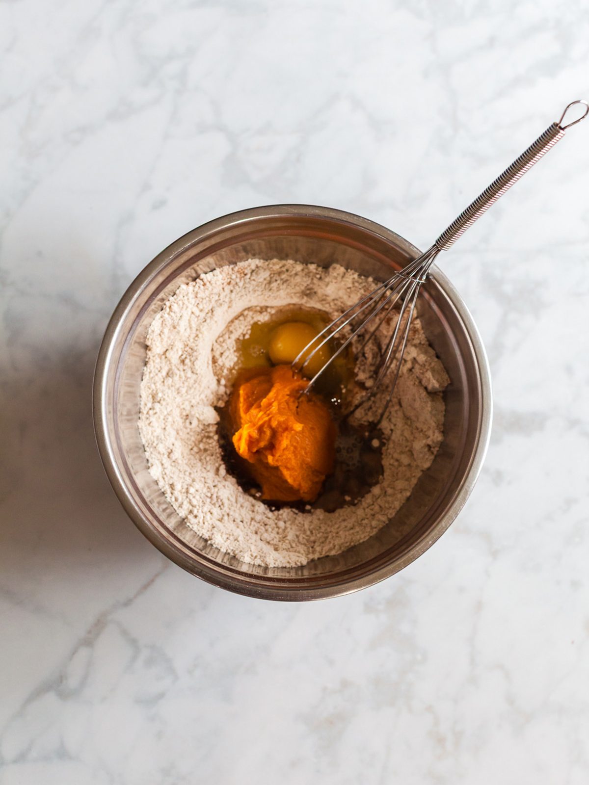 Pumpkin puree, egg, maple syrup, and vanilla added to dry mixture in a bowl for pumpkin spice breakfast cookie dough.