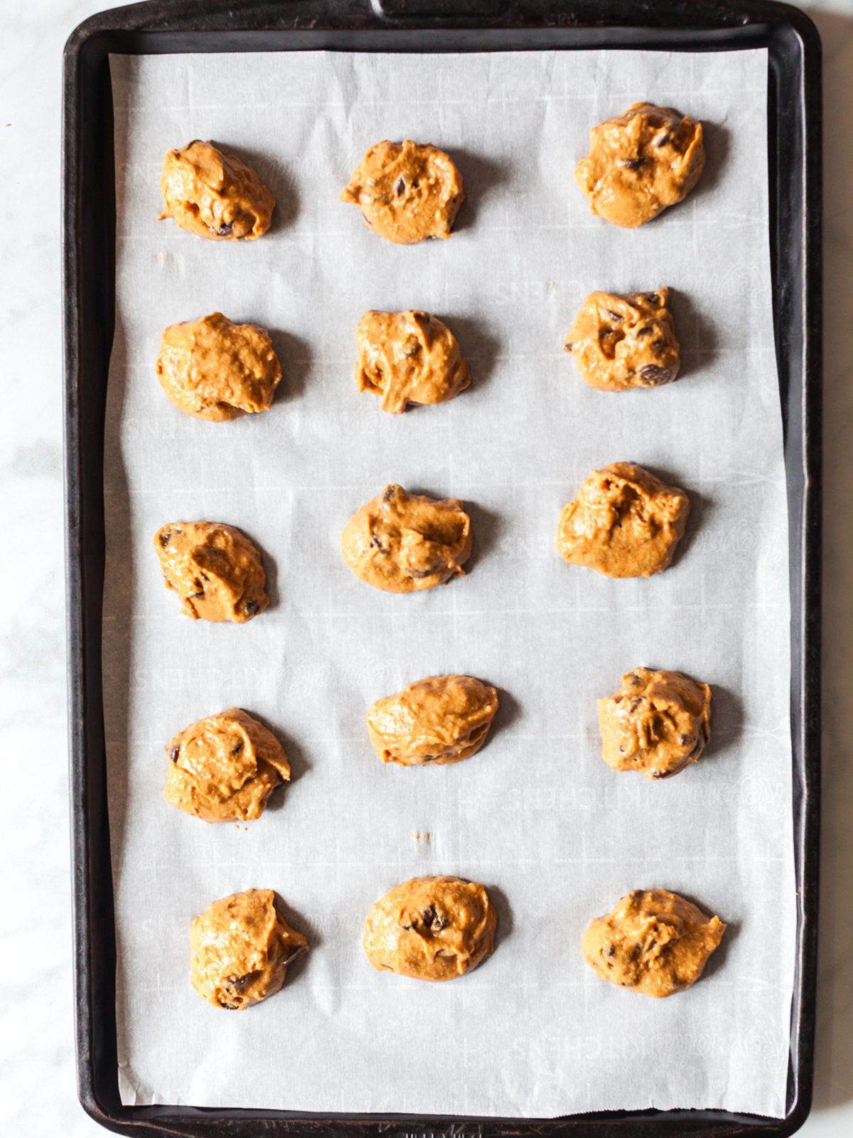 Scoops of pumpkin cookie dough spaced on a parchment-lined baking sheet ready to bake healthy pumpkin breakfast cookies.