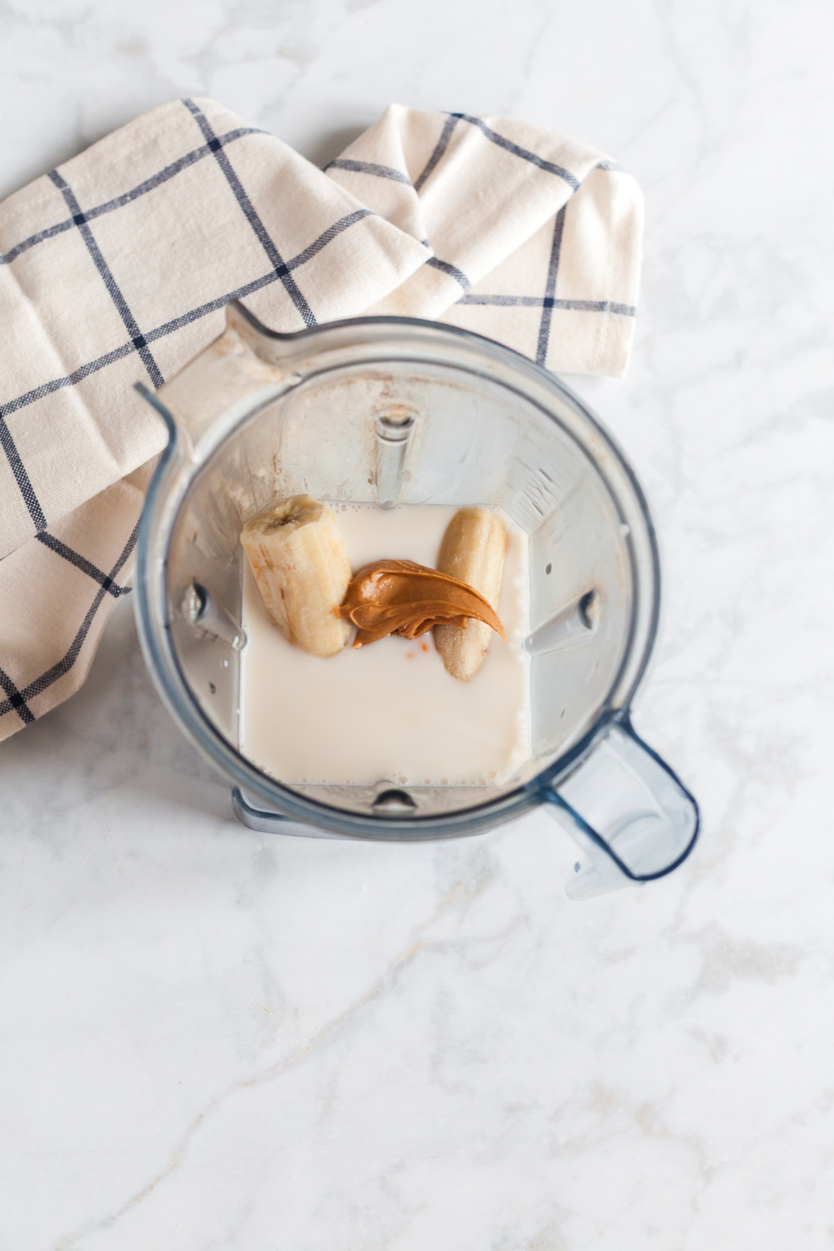 Overhead view of a blender filled with bananas, peanut butter, pumpkin and milk, ready to blend for a pumpkin smoothie.