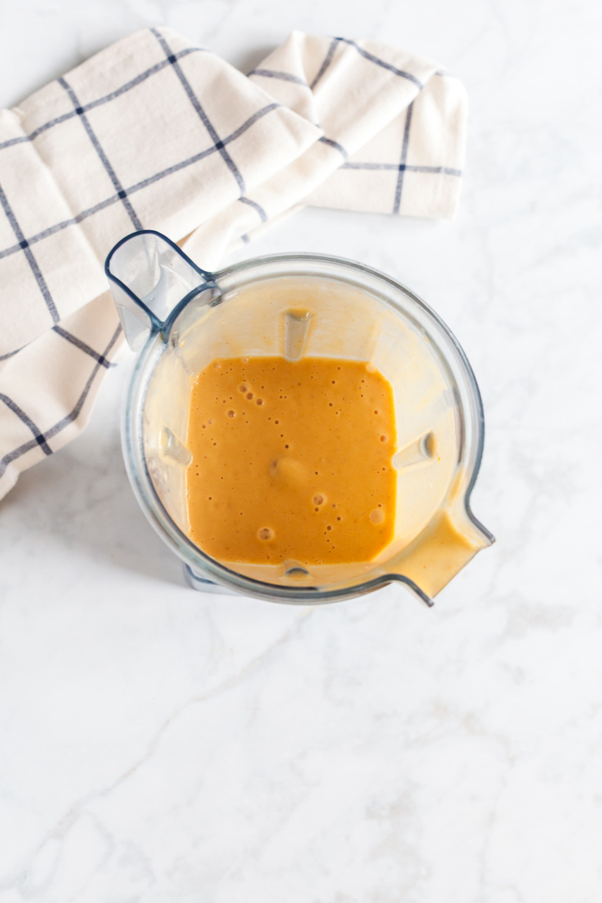 Freshly blended pumpkin smoothie mixture in a blender on a marble counter.