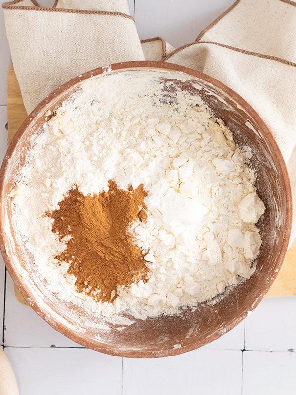 Mixing dry ingredients for pumpkin streusel bread including flour, baking powder, and cinnamon in a large wooden bowl with a whisk on the side.