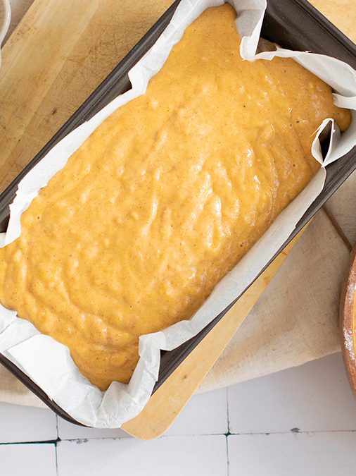 Pumpkin bread batter poured into a parchment-lined loaf pan with streusel topping mixture set to the side.