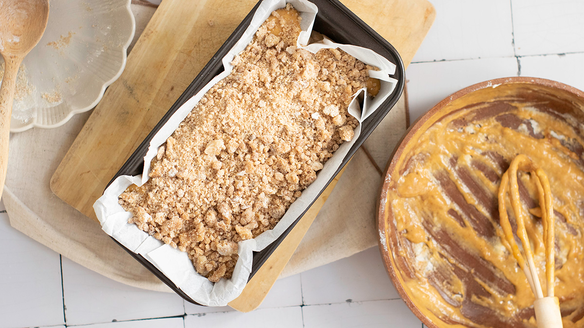 Loaf pan filled with pumpkin bread batter topped with crumbly streusel, ready to bake in the oven.