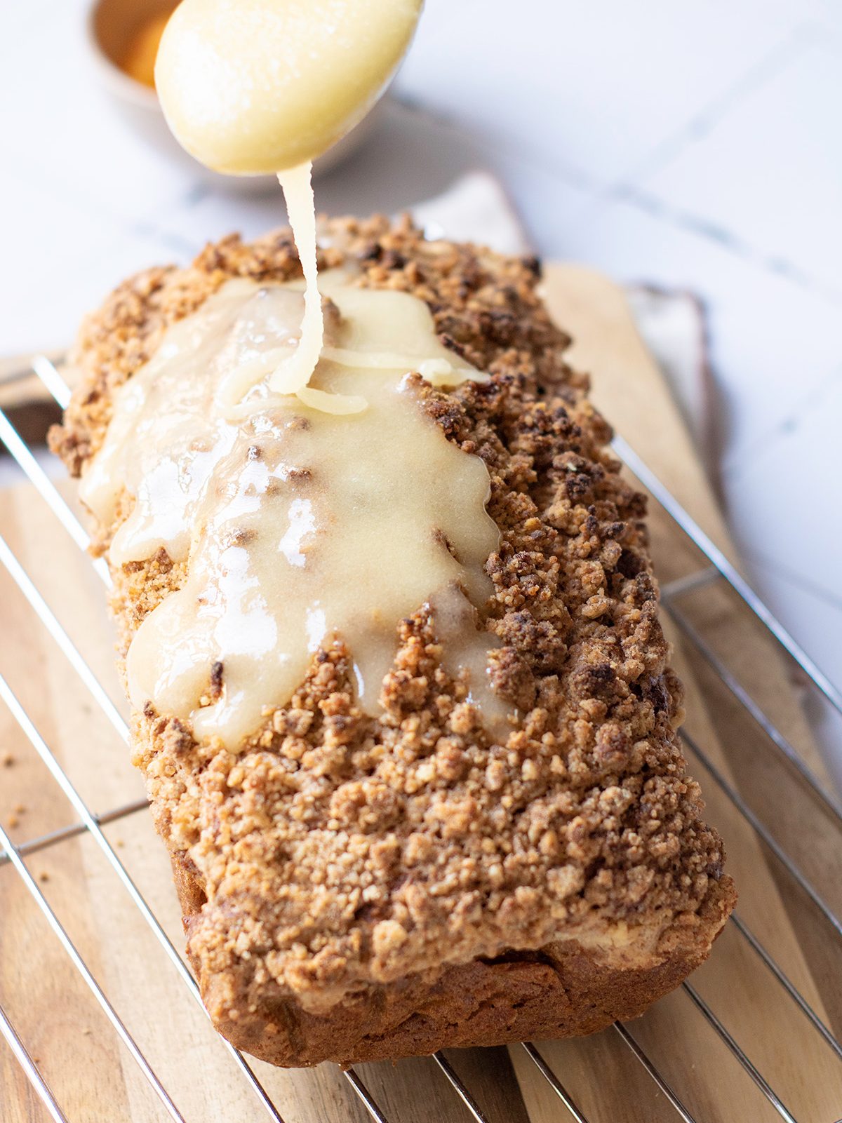 Warm pumpkin streusel bread cooling on a wire rack while being drizzled with golden honey glaze from a spoon.