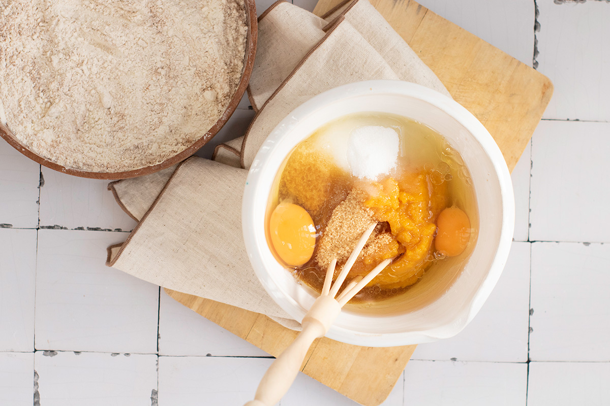 Wet ingredients including eggs, pumpkin puree, sugars, and oil combined in a white bowl before mixing for pumpkin bread batter.