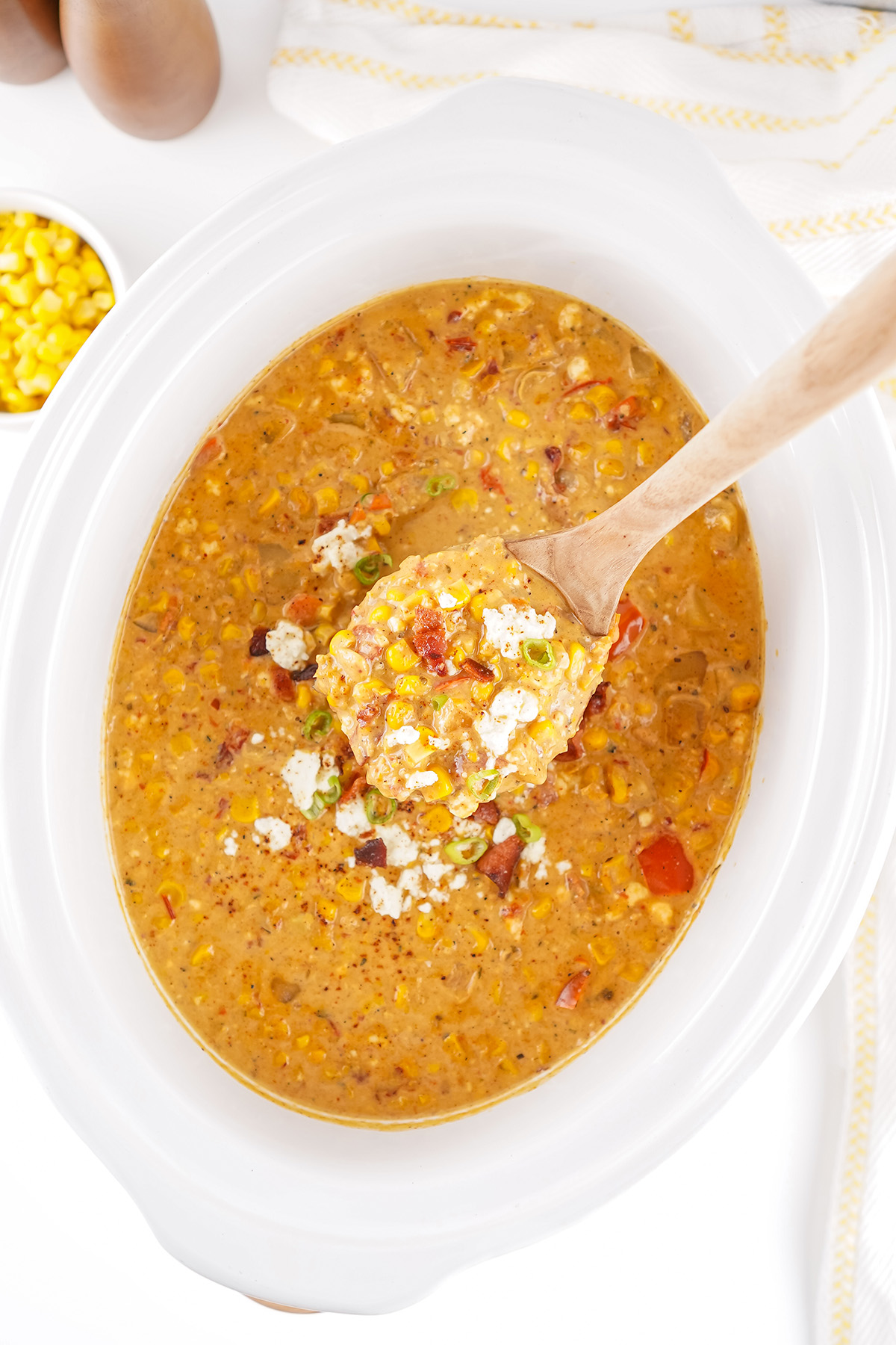 A look inside a slow cooker filled with creamy Mexican street corn soup, showing chunks of potatoes, corn, and red peppers mixed with cheese and bacon.