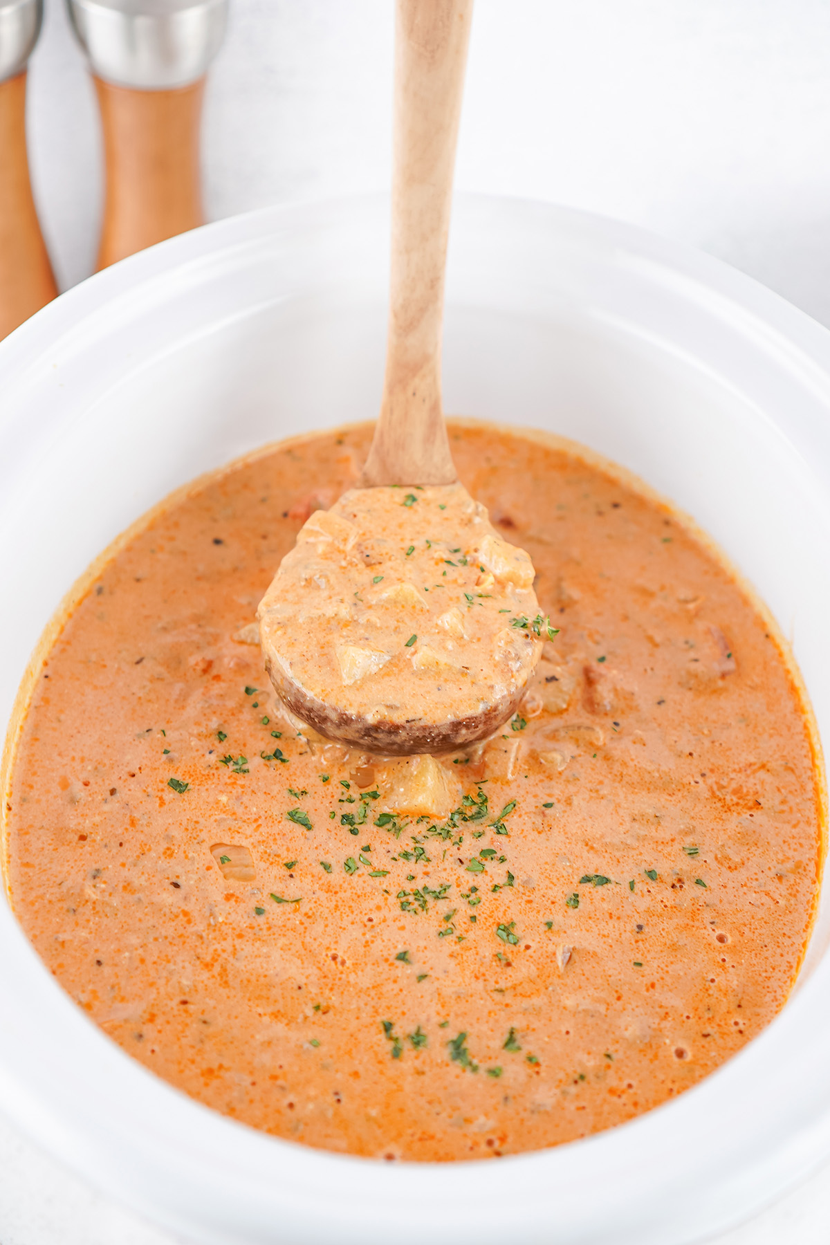 Top view of a ladle dipping into creamy slow cooker sausage potato soup with visible potatoes and sausage pieces.
