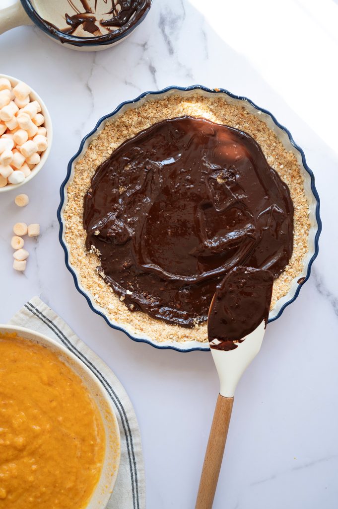 Melted dark chocolate being spread evenly over the graham cracker crust with a spatula for the chocolate base layer.