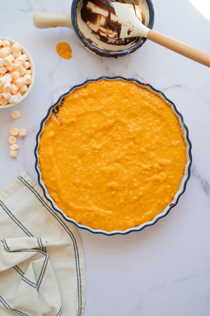 Pie dish filled with smooth sweet potato filling spread over the chocolate layer, ready for marshmallows.