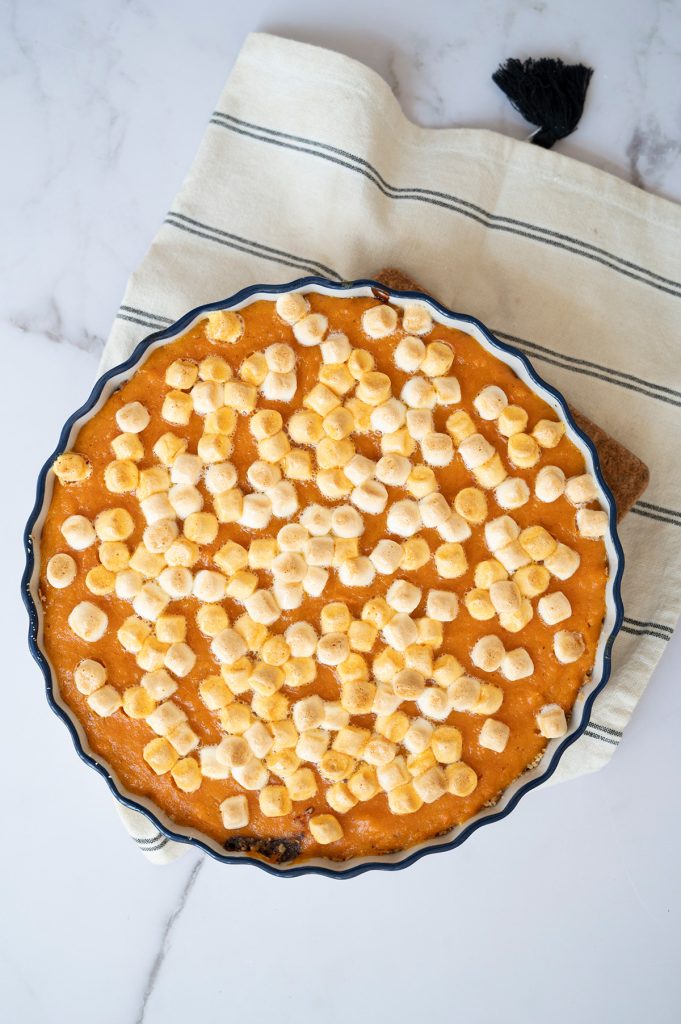 Overhead view of baked sweet potato s’mores pie with toasted mini marshmallows on top, cooling on a striped towel.
