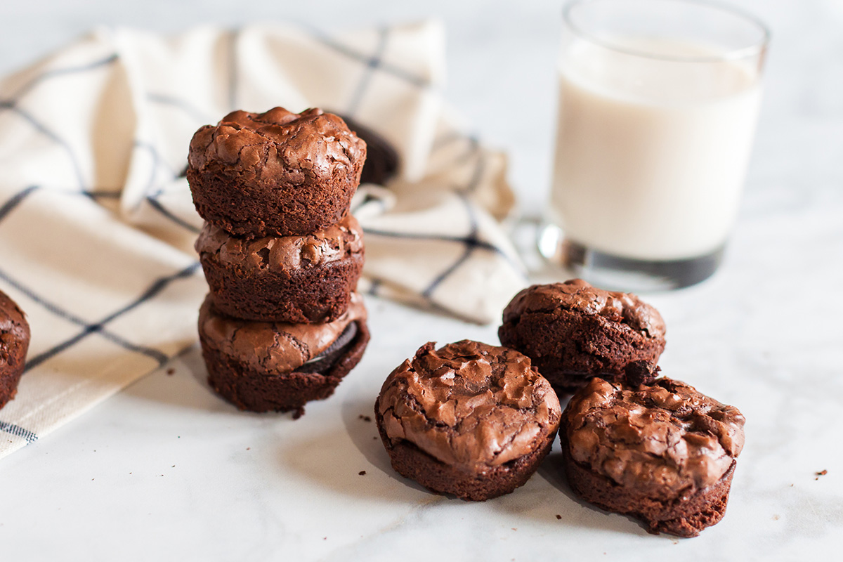 Oreo-stuffed brownie cups stacked beside loose oreo stuffed brownies and a glass of milk.