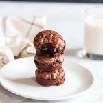 Stack of three Oreo-stuffed brownie cups on a white plate with a glass of milk in the background.