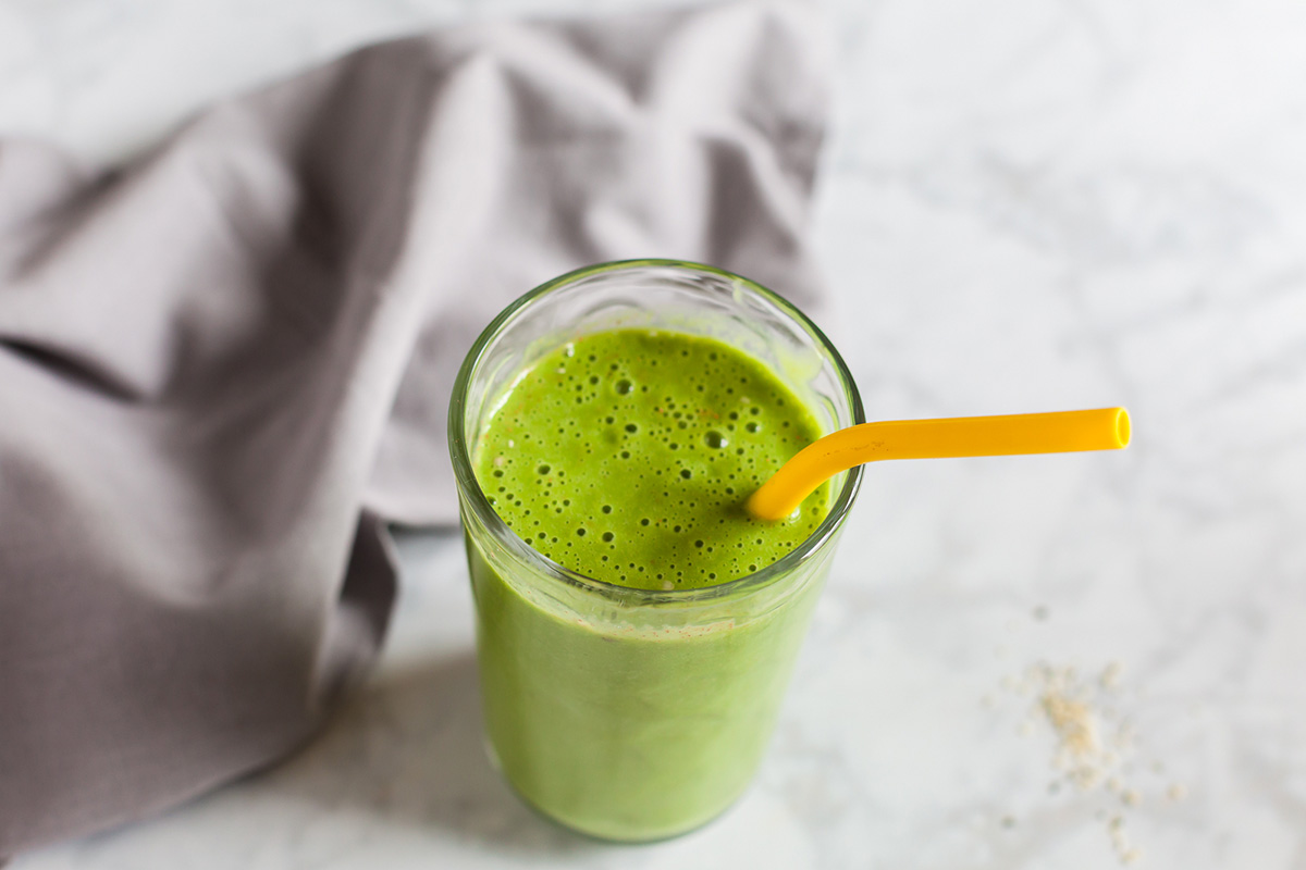 Smooth and creamy green pear smoothie with yellow straw on marble counter, gray napkin in background.