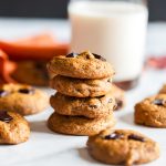 Stack of soft pumpkin oat breakfast cookies with dark chocolate chunks beside a glass of milk and an orange napkin, a cozy fall breakfast treat.
