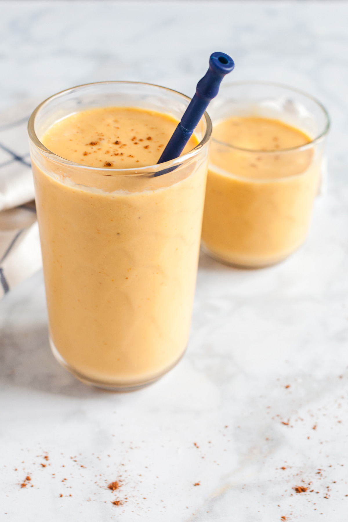 Two glasses of pumpkin smoothies topped with pumpkin pie spice, served with straws on a marble counter.