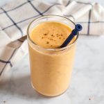 Overhead shot of a pumpkin smoothie in a glass with pumpkin pie spice sprinkled on top and a straw.