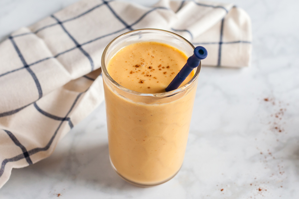 Overhead shot of a pumpkin smoothie in a glass with pumpkin pie spice sprinkled on top and a straw.