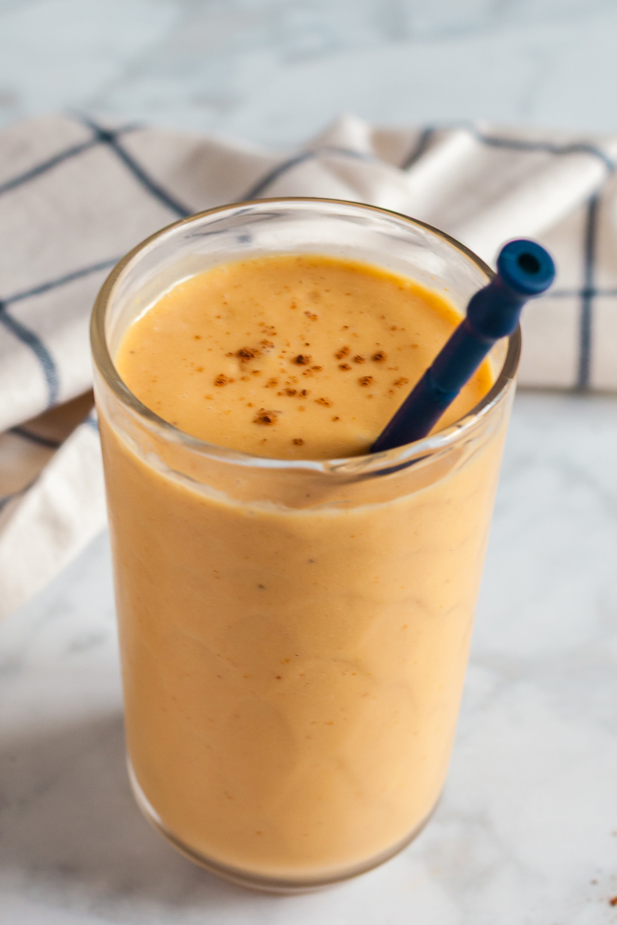 Glass of creamy pumpkin smoothie topped with a sprinkle of pumpkin pie spice and served with a straw.