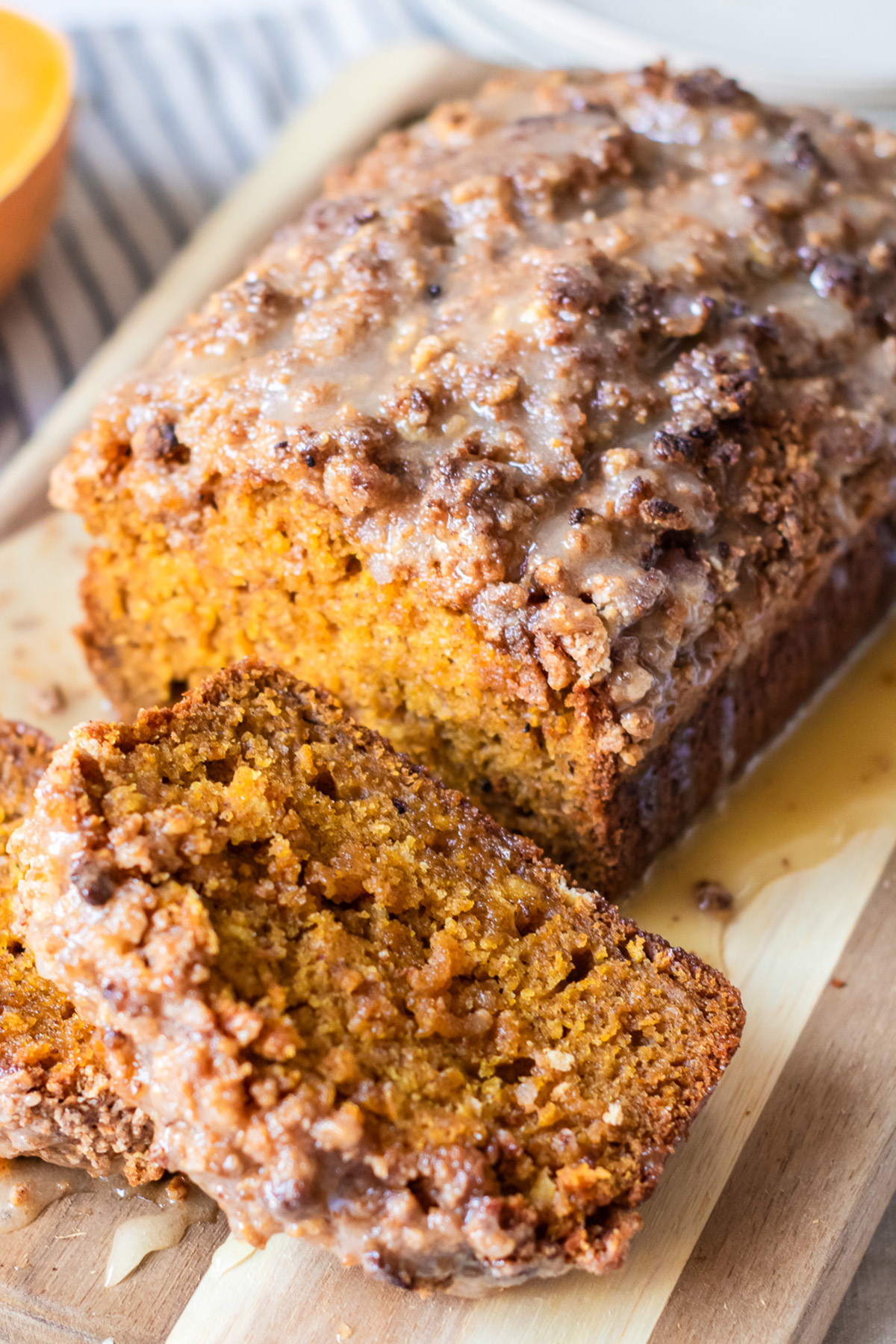 Close-up of moist pumpkin streusel bread with a crunchy crumble topping and shiny honey glaze, sliced on a wooden cutting board.
