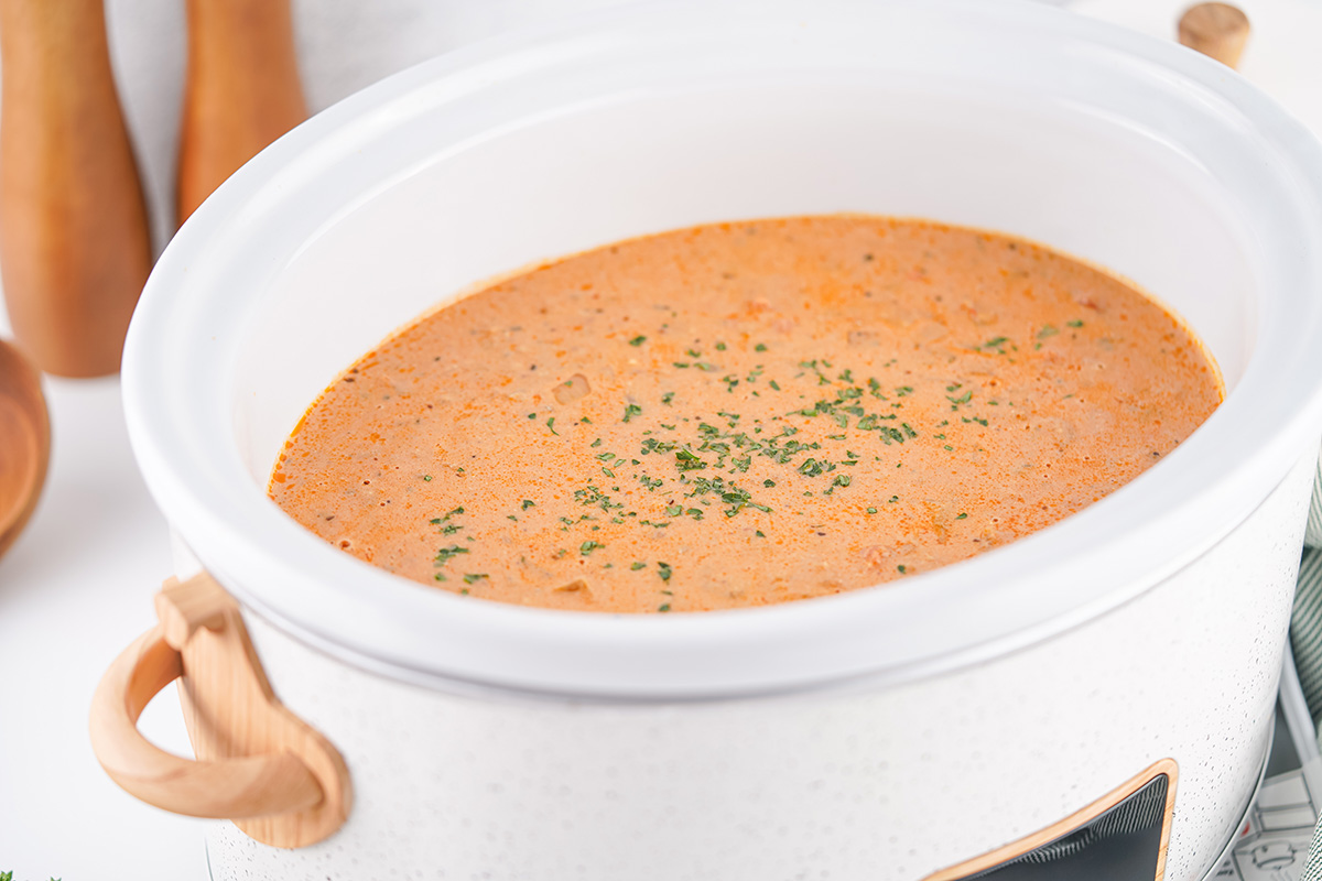 Side view of a crockpot filled with creamy sausage potato soup topped with fresh parsley.