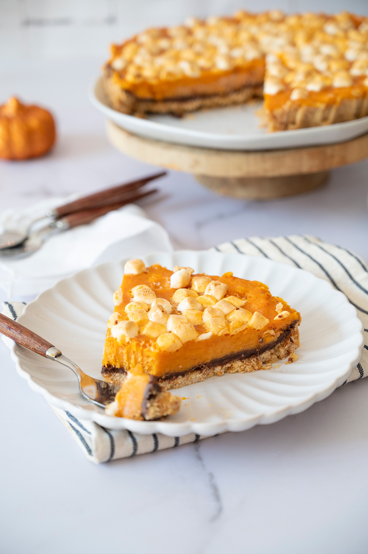 Close-up side view of a sweet potato pie slice showing the layers of graham cracker crust, melted chocolate, and creamy sweet potato filling topped with toasted mini marshmallows.