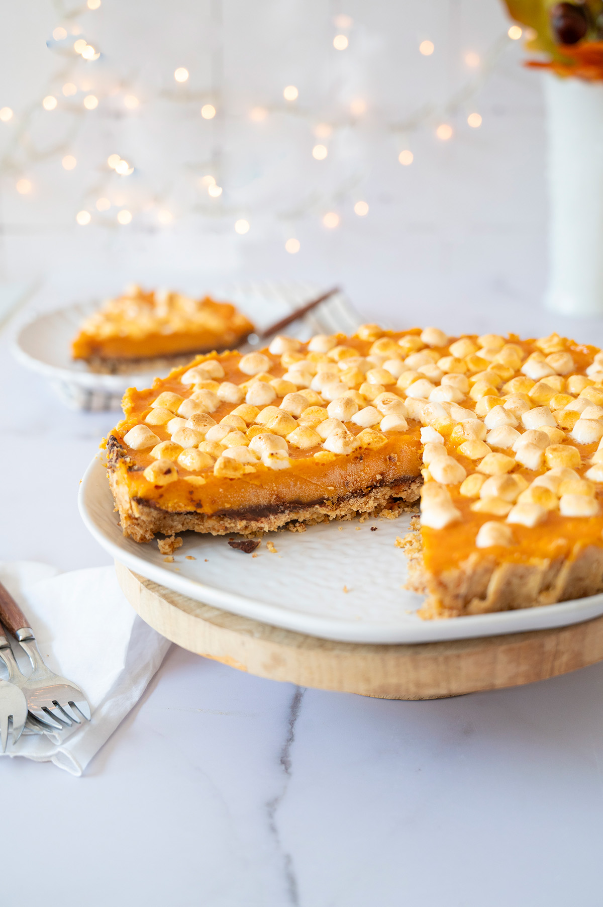 Sweet potato pie with toasted marshmallow topping on a white plate and wooden stand, with one slice removed to reveal the dark chocolate layer.