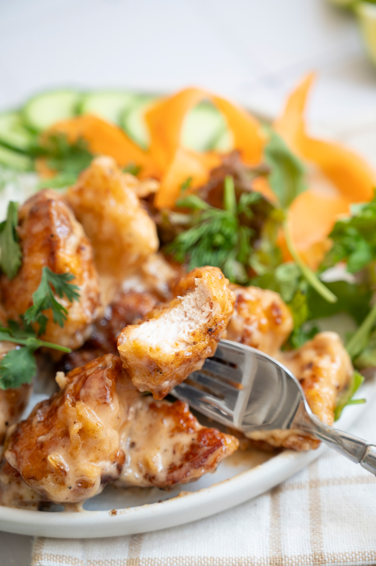 Fork lifting a piece of sauced bang bang chicken to show the juicy, cooked-through center with crispy edges.