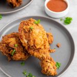 Crispy buttermilk fried chicken drumsticks served on a gray plate with fresh parsley.