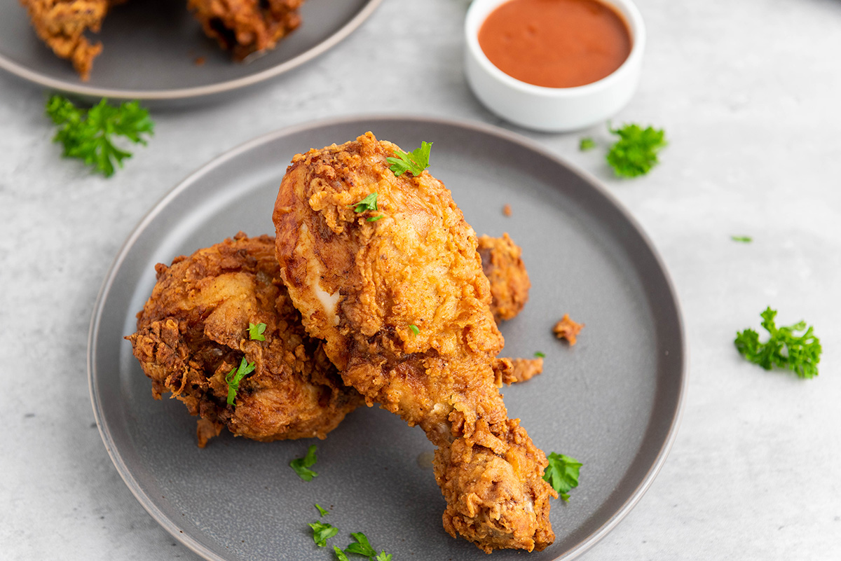 Crispy buttermilk fried chicken drumsticks served on a gray plate with fresh parsley.