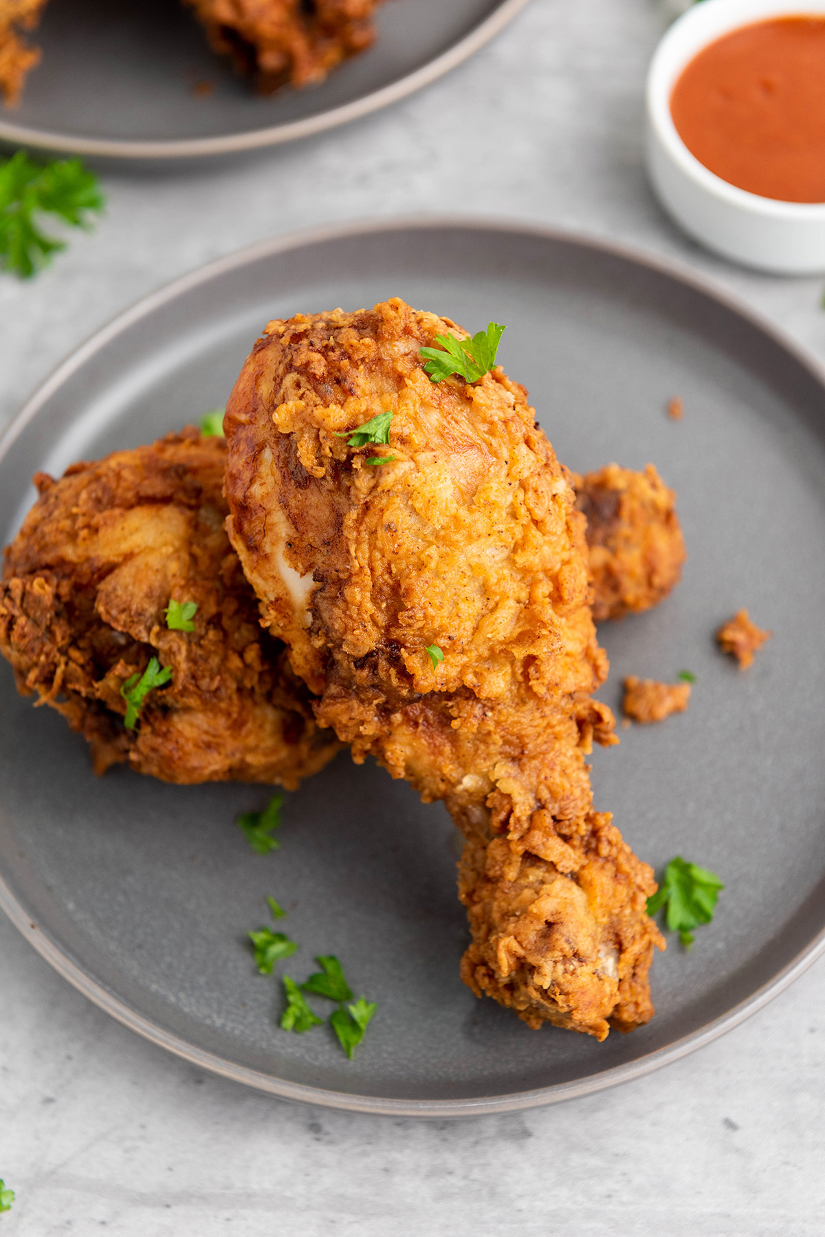 Close-up of crunchy buttermilk fried chicken drumsticks on a gray plate.