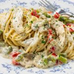 Plate of chicken mushroom alfredo pasta with creamy sauce, asparagus, and red bell pepper, garnished with parsley and a fork on the side.