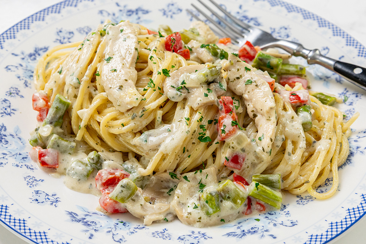 Plate of chicken mushroom alfredo pasta with creamy sauce, asparagus, and red bell pepper, garnished with parsley and a fork on the side.