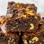 Fudgy chocolate walnut brownies stacked on a plate, showing rich chocolate texture and chunks of walnuts inside.