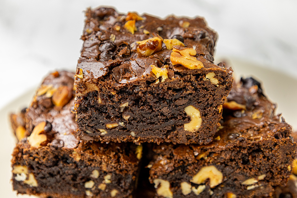 Fudgy chocolate walnut brownies stacked on a plate, showing rich chocolate texture and chunks of walnuts inside.