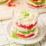 Festive layered trifle in a clear glass showing red velvet, green cake, and cream layers.