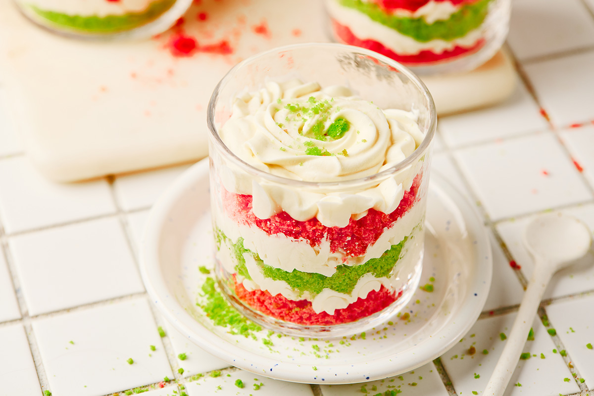 A fun and festive Christmas trifle dessert made with crumbled red and green cakes and an easy, fluffy cream cheese filling that tastes like the holidays in every bite. Festive layered trifle in a clear glass showing red velvet, green cake, and cream layers.