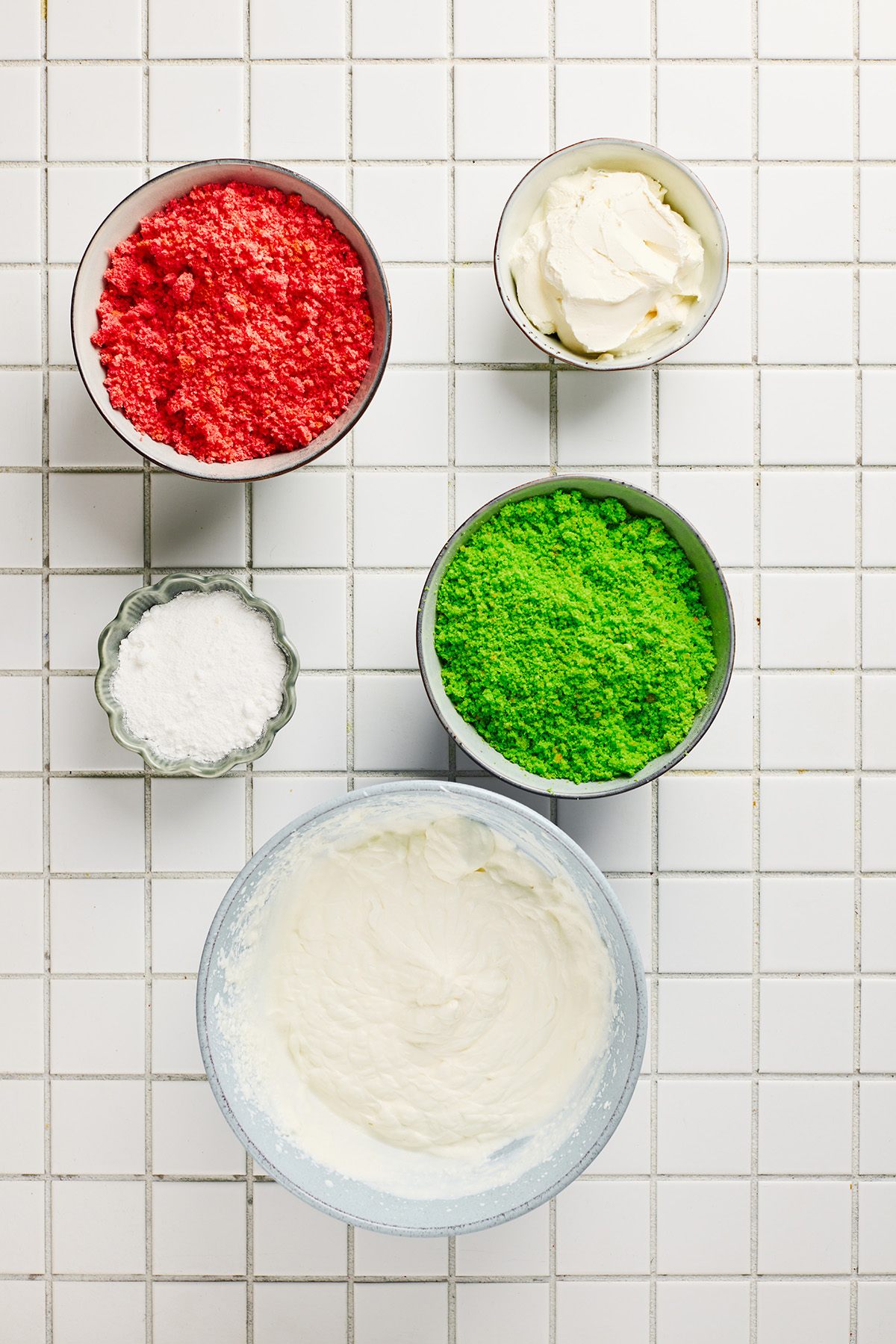 A fun and festive Christmas trifle dessert made with crumbled red and green cakes and an easy, fluffy cream cheese filling that tastes like the holidays in every bite. Bowls of red and green cake crumbs with cream cheese, powdered sugar, and whipped cream filling