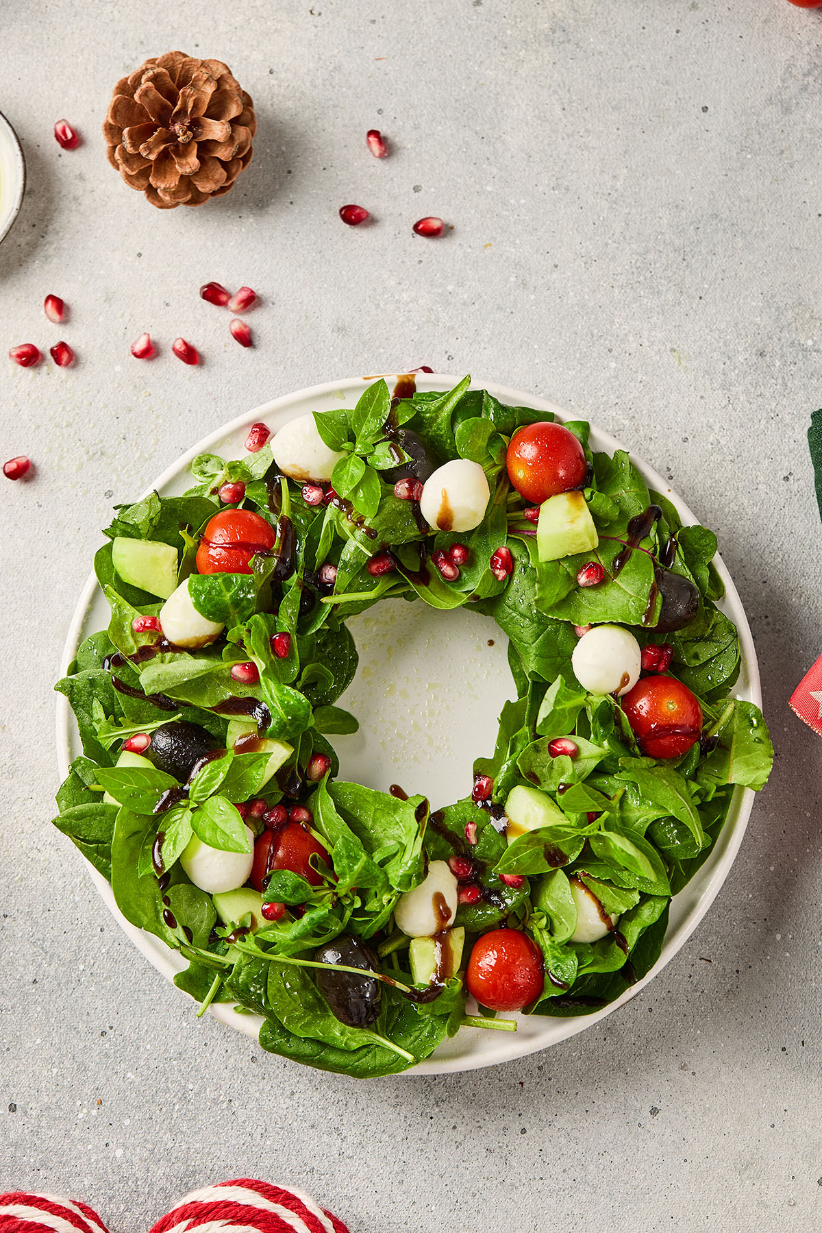 Christmas wreath salad made with mixed greens, cherry tomatoes, mozzarella balls, cucumbers, olives, and pomegranate seeds arranged in a circular wreath shape.