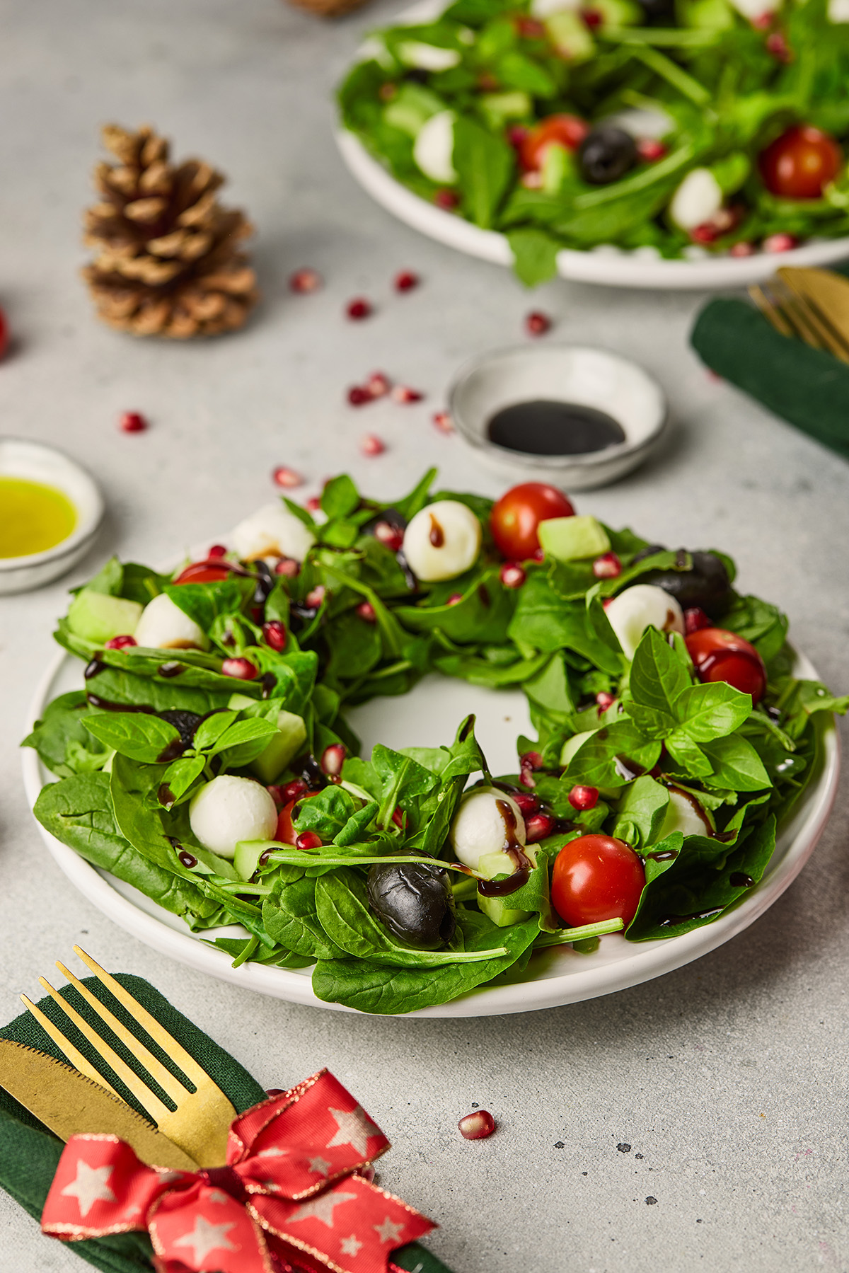 Holiday wreath salad featuring fresh greens, tomatoes, mozzarella, olives, cucumbers, and pomegranate seeds drizzled with balsamic glaze.
