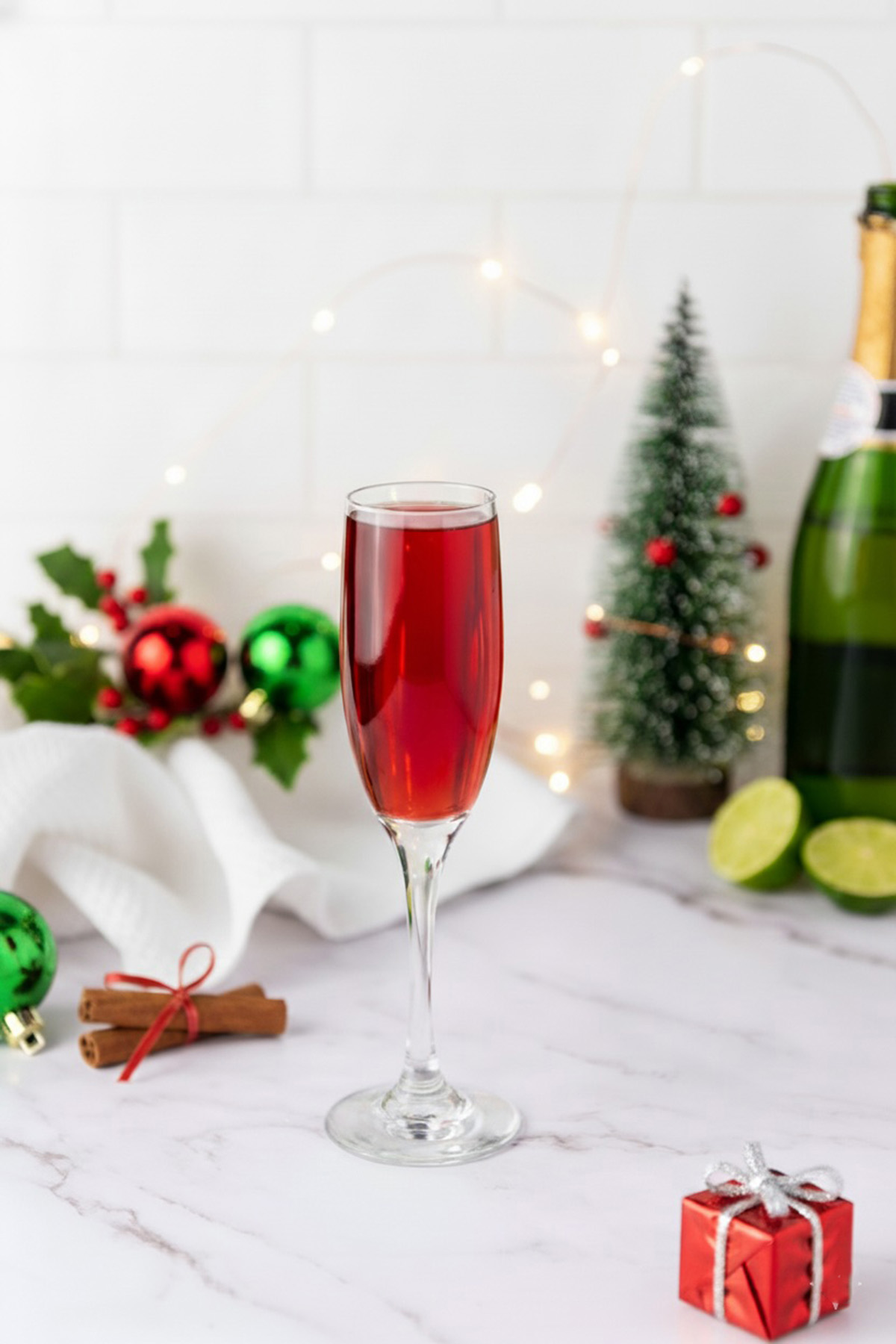 Tall champagne flute filled with cranberry mimosa with a champagne bottle in the background surrounded by Christmas decor.