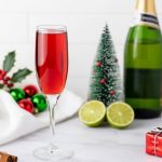 Champagne flute filled with a bright red cranberry mimosa on a white marble surface surrounded by holiday decor.