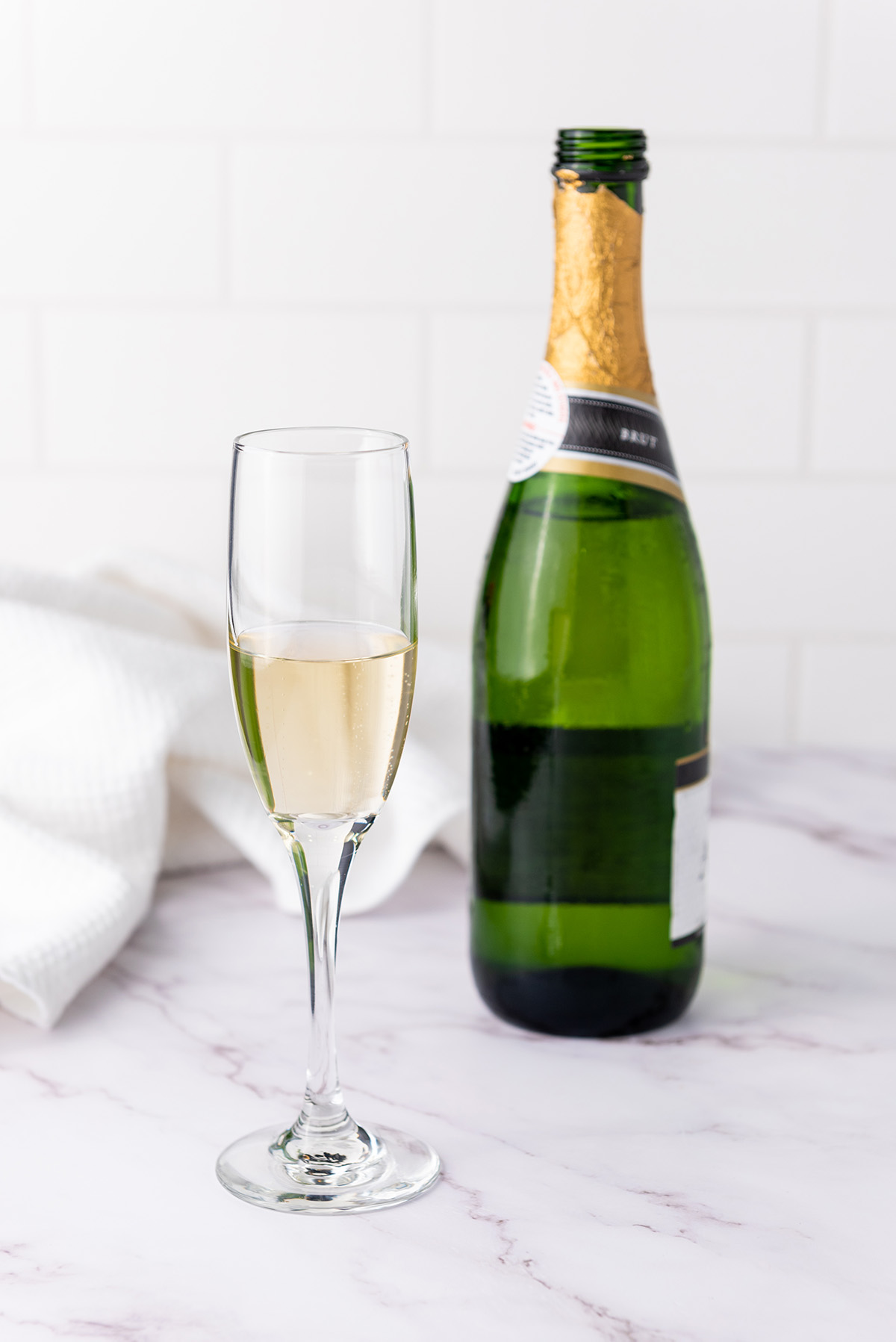 Champagne flute with chilled brut champagne next to an open champagne bottle on a white marble counter.