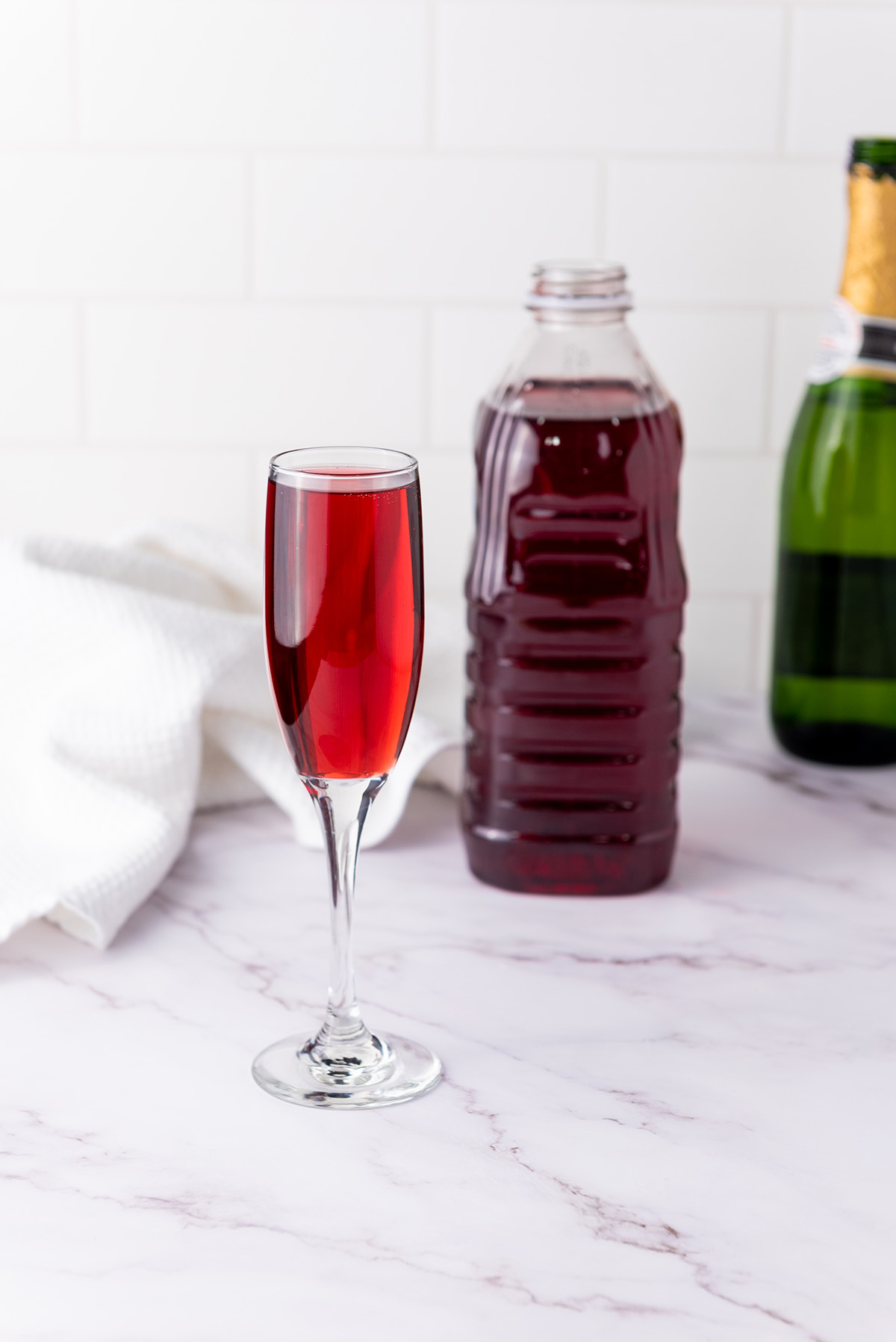 Cranberry mimosa in a champagne flute with a bottle of cranberry juice and champagne in the background.