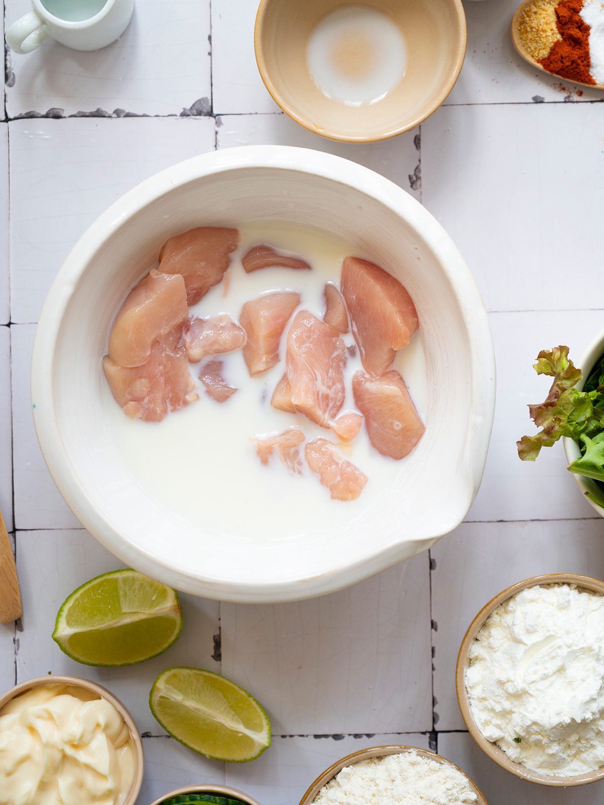 Raw chicken pieces soaking in buttermilk in a ceramic bowl as part of the marinating step.