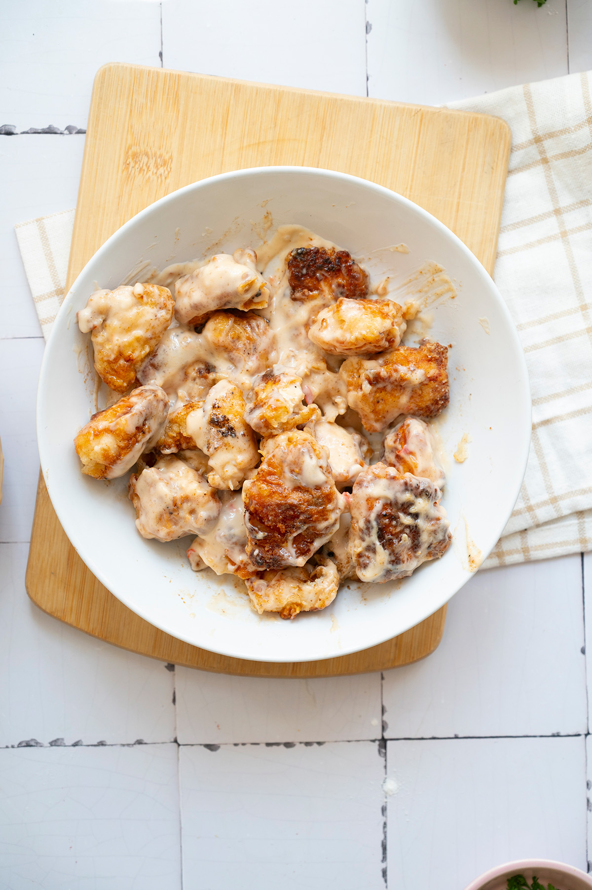 Crispy fried chicken pieces tossed in creamy bang bang sauce in a white bowl.