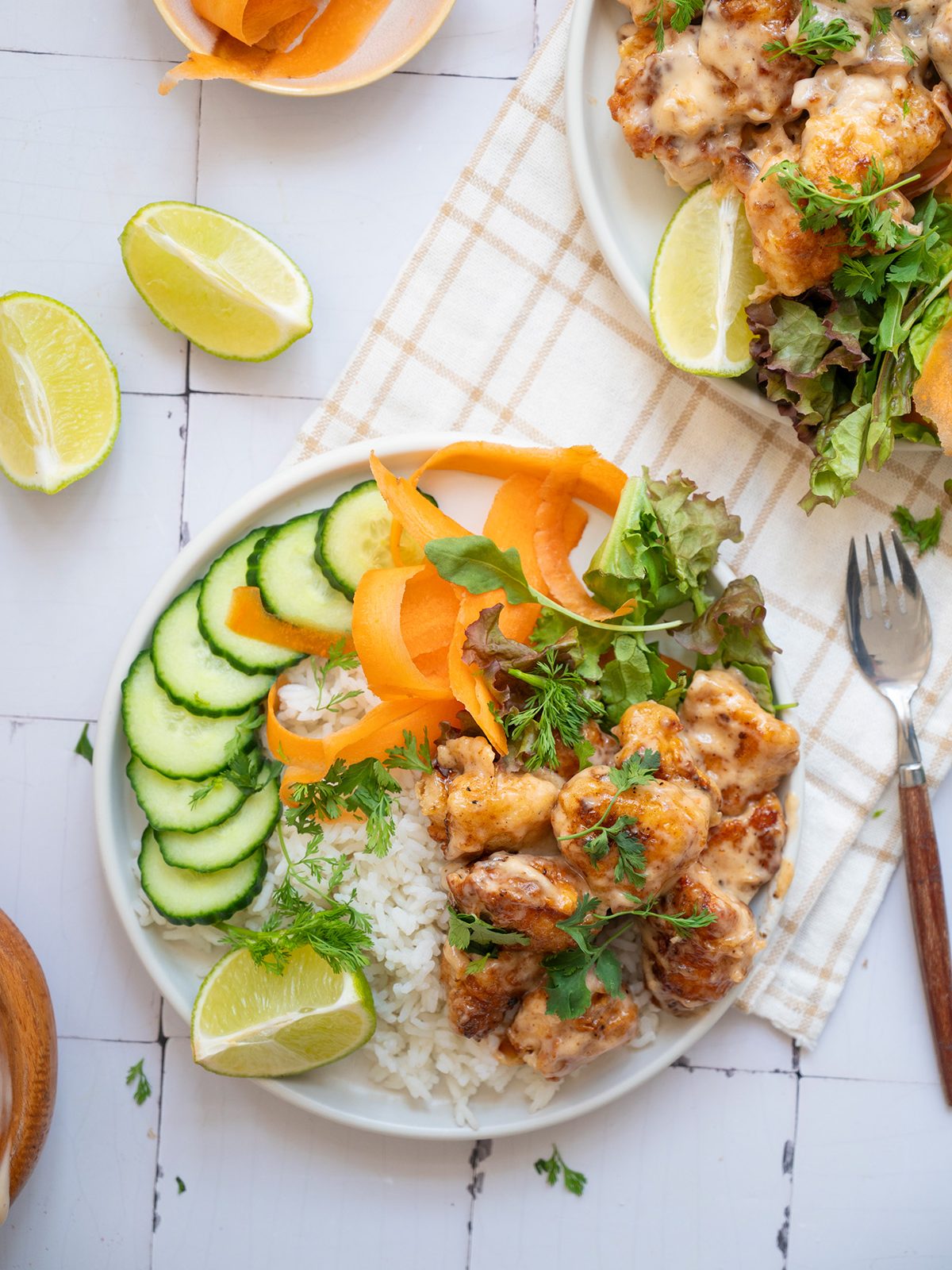 Bang bang chicken rice bowl with white rice, cucumber slices, carrot ribbons, mixed greens, and sauced chicken topped with fresh cilantro.