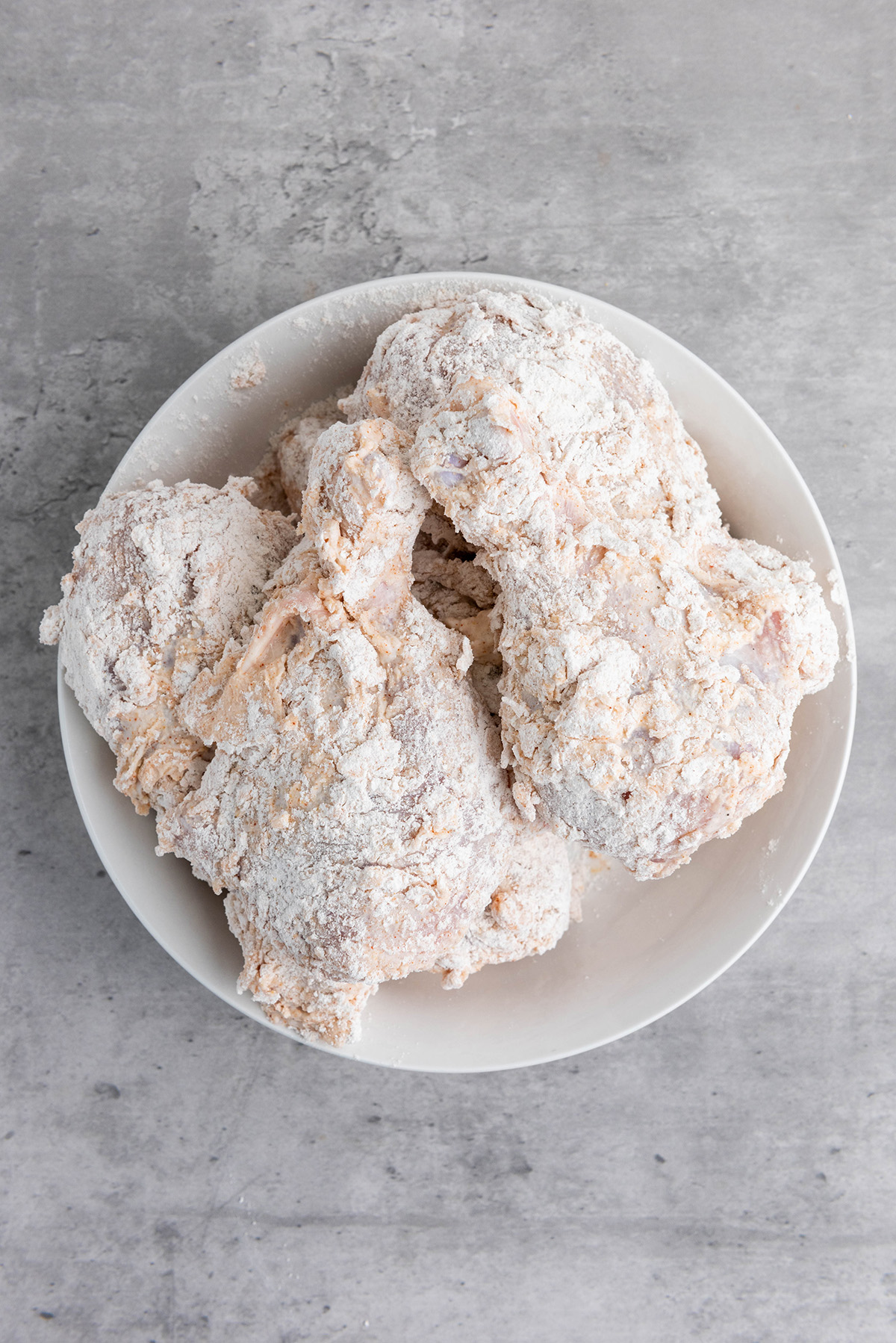 Chicken drumsticks coated in seasoned flour before frying.