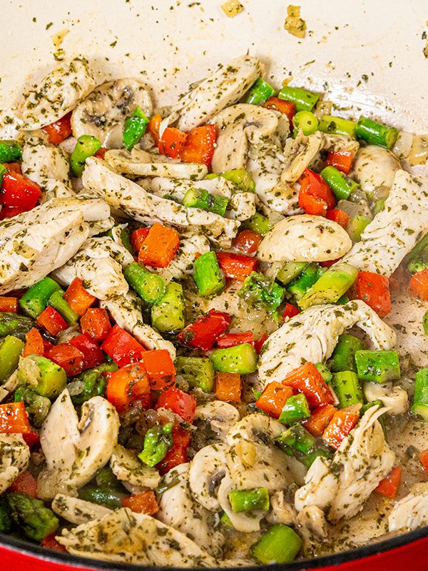 Chicken cooking with mushrooms, asparagus, and red bell pepper in the skillet.