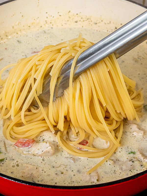 Cooked spaghetti being added to the creamy chicken mushroom alfredo sauce.