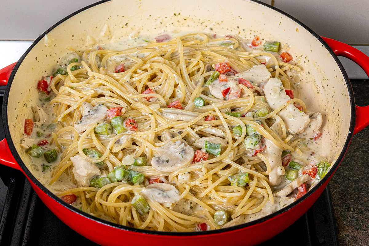 Chicken mushroom alfredo pasta stirred together in a red skillet until coated in creamy sauce.